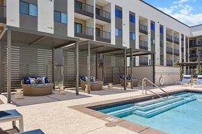 Gilbert apartment for rent - A swimming pool is surrounded by sun loungers and a building with balconies.