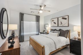 Gilbert apartment for rent - A bedroom with a large bed, a ceiling fan, and a nightstand with a lamp.