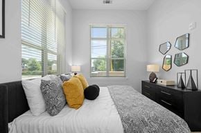 Charlotte apartment for rent - A bedroom with a large bed, a window with blinds, and a black dresser with a mirror.