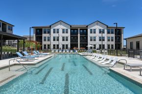 San Antonio apartment for rent - A large swimming pool in front of a multi-story building with lounge chairs around it.
