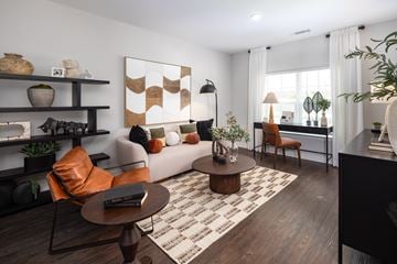 Fairburn apartment for rent - A living room with a brown and white rug, a brown coffee table, a white sofa, a brown chair, a black bookshelf, and a painting on the wall.