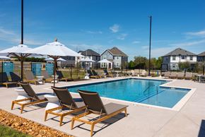 Leander apartment for rent - A pool with chairs and umbrellas in front of a row of houses.