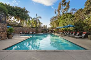 Carlsbad apartment for rent - A large outdoor swimming pool surrounded by trees and lounge chairs.