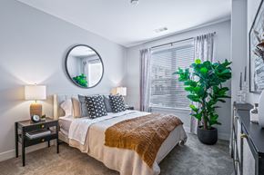 Huntsville apartment for rent - A bedroom with a bed, nightstand, and a plant.