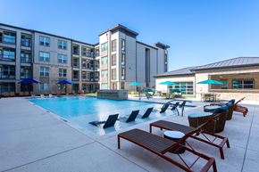 Prosper apartment for rent - A swimming pool surrounded by lounge chairs and umbrellas in front of a building.