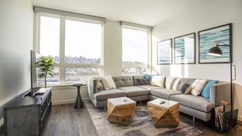 A living room with a grey couch, a wooden coffee table, and a large window.