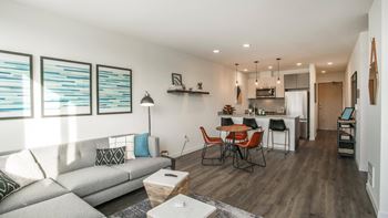 A modern living room with a grey sofa and a wooden dining table.