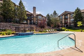 Aurora apartment for rent - A swimming pool surrounded by a metal fence and a stone wall with a building in the background.
