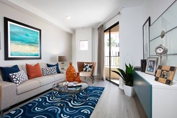 Long Beach apartment for rent - A living room with a grey couch, a blue patterned rug, and a painting of a beach scene on the wall.