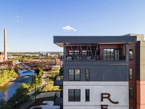 Denver apartment for rent - A modern building with the letter R on it is in the foreground with a river and bridge in the background.