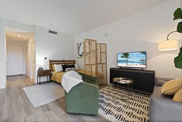 Philadelphia apartment for rent - A modern living room with a grey sofa, a green armchair, a wooden side table, and a television displaying a beach scene.