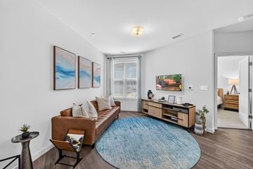 Hackensack apartment for rent - A living room with a brown couch, a blue rug, and a painting on the wall.
