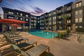 Tempe apartment for rent - A pool area with lounge chairs and umbrellas in front of apartment buildings.