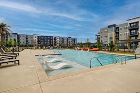 Baton Rouge apartment for rent - A swimming pool with a slide and a bench in front of apartment buildings.