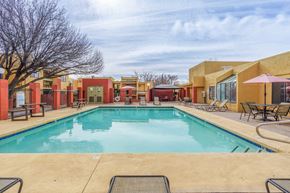 Rio Rancho apartment for rent - A large outdoor swimming pool surrounded by lounge chairs and umbrellas.