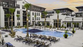 Charleston apartment for rent - A large pool surrounded by lounge chairs and umbrellas in front of a multi-story building.