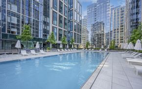 Boston apartment for rent - an outdoor swimming pool with chaise lounge chairs and trees in front of a tall building