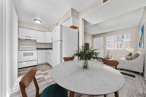 Tucson apartment for rent - Dining area next to a white kitchen with wood flooring and natural light.