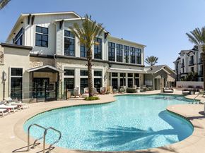 Chula Vista apartment for rent - A large swimming pool is in front of a two-story building with a palm tree in front of it.