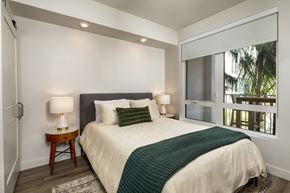 Los Angeles apartment for rent - A bedroom with a bed, a nightstand with a lamp, and a window with a view of trees.