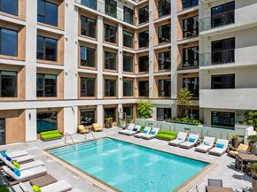 Culver City apartment for rent - A large swimming pool surrounded by lounge chairs in front of a multi-story building.