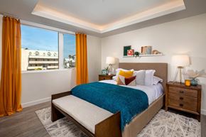 Culver City apartment for rent - A bedroom with a large bed, a window with orange curtains, and a wooden nightstand with a lamp.