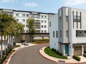 Escondido apartment for rent - A white building with a blue door is situated on the right side of a curved driveway.