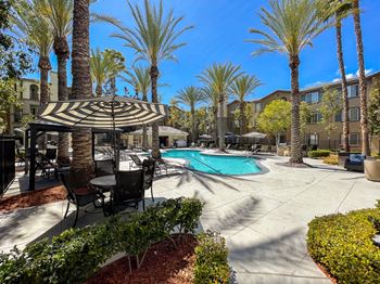 Swimming pool with tables and umbrellas in a courtyard with palm trees