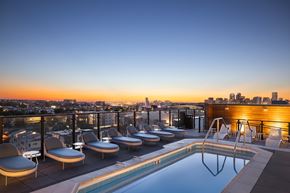 Denver apartment for rent - A rooftop pool with lounge chairs overlooking a city skyline at dusk.