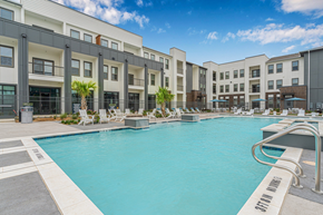 Denton apartment for rent - A swimming pool in front of a building with lounge chairs around it.