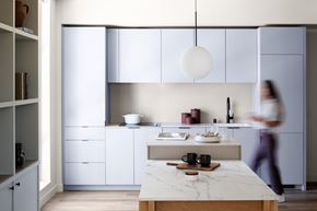 Seattle apartment for rent - A woman is walking in a modern kitchen with white cabinets and a marble island.