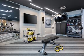 Oakland apartment for rent - a spacious fitness center with a large tv and weights on the wall