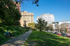 San Francisco apartment for rent - people sitting on a bench in a park with tall buildings in the background