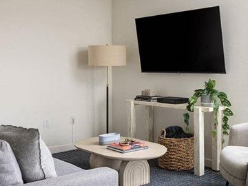 Long Beach apartment for rent - A living room with a grey couch, a white table, a lamp, a plant, and a television mounted on the wall.
