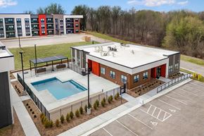 Rochester apartment for rent - A building with a red and grey exterior has a pool in front of it.