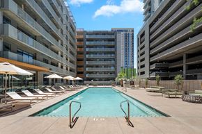 Phoenix apartment for rent - A large swimming pool surrounded by lounge chairs and umbrellas in front of apartment buildings.
