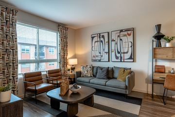Golden apartment for rent - A living room with a grey couch, a brown chair, a coffee table, and a painting on the wall.