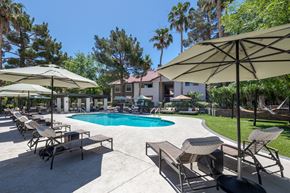 Henderson apartment for rent - Umbrellas and patio chairs surrounding a community swimming pool at Sage at Green Valley apartments in Henderson, NV.