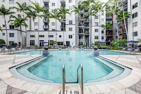 Fort Lauderdale apartment for rent - A swimming pool in front of a building with palm trees.