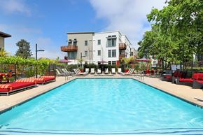 Santa Rosa apartment for rent - A large swimming pool in front of a building with red lounge chairs on the side.