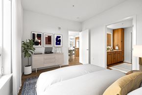 Seattle apartment for rent - A white bedroom with a bed in the foreground and a desk with a laptop and a plant on it.