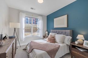 Rochester apartment for rent - A bedroom with a bed, nightstand, and a window with a view of a building outside.