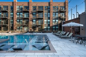 Arvada apartment for rent - A large swimming pool in front of a brick building with lounge chairs and umbrellas.