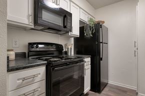 San Antonio apartment for rent - A black refrigerator stands in a kitchen with white cabinets and a black stove.