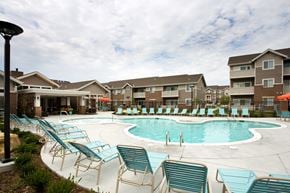 Wichita apartment for rent - A swimming pool surrounded by chairs and buildings in the background.