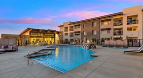 Mesa apartment for rent - A large swimming pool is surrounded by lounge chairs and umbrellas in a courtyard.