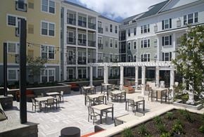 Ronkonkoma apartment for rent - A patio with tables and chairs is surrounded by apartment buildings.