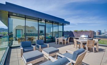 Modern outdoor seating area with wooden furniture and glass walls overlooking a cityscape.