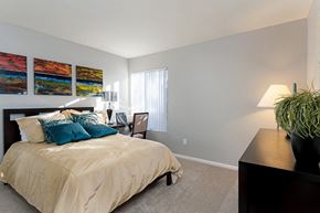 San Diego apartment for rent - A bedroom with a bed, nightstand, lamp, and a plant at The Casas Apartments, San Diego, CA