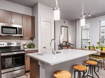 Fort Worth apartment for rent - A modern kitchen with a stainless steel oven and microwave, a white countertop, and wooden bar stools.
